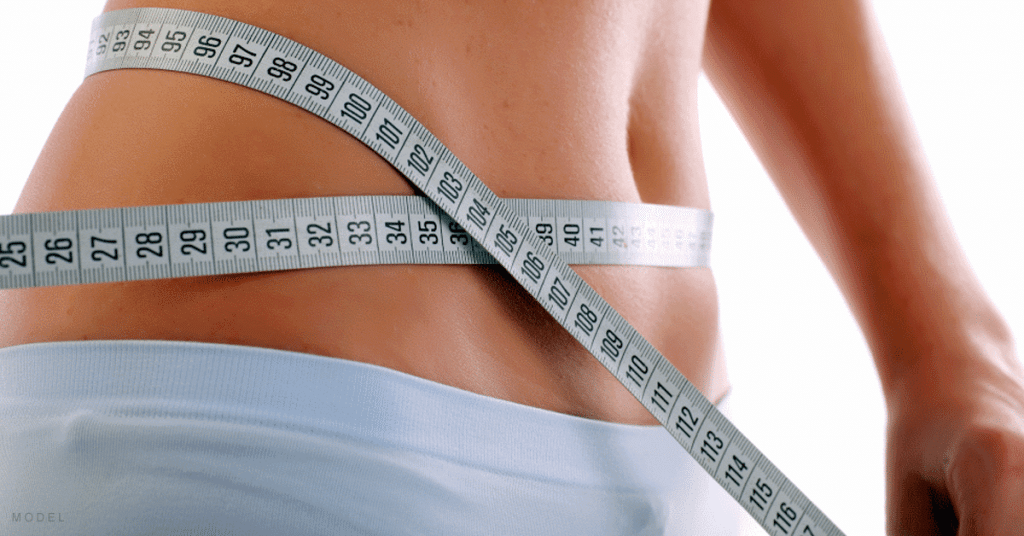 A person considering an tummy tuck measures their waistline.