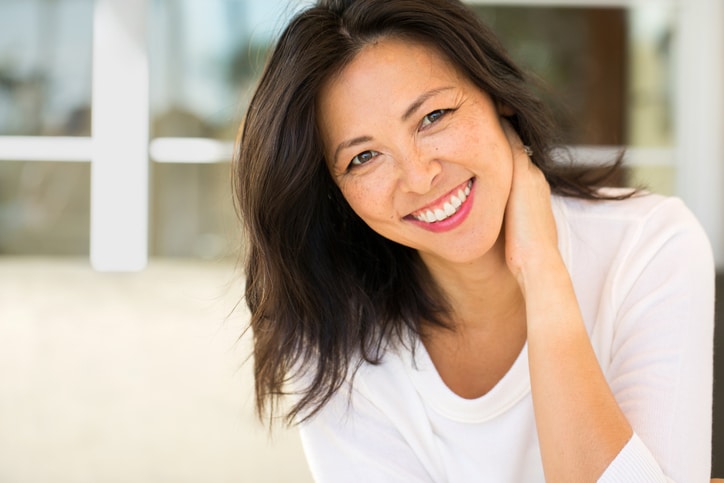 A middle-aged woman smiling and resting her arm on her neck.