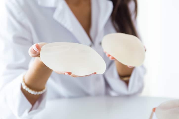 A woman holding two different breast implants.