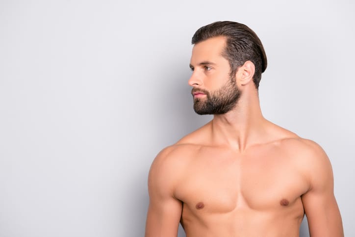 A man with a bare chest is pictured from the chest up posing while looking off to the side in front of a gray background