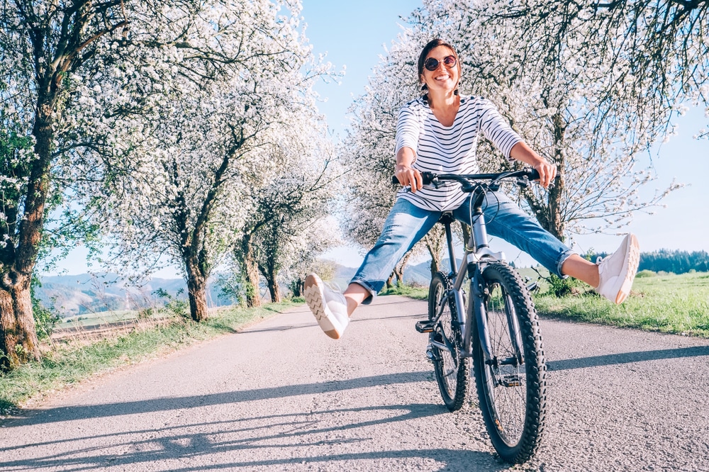 A woman playfully rides a bicycle down a country road in the springtime